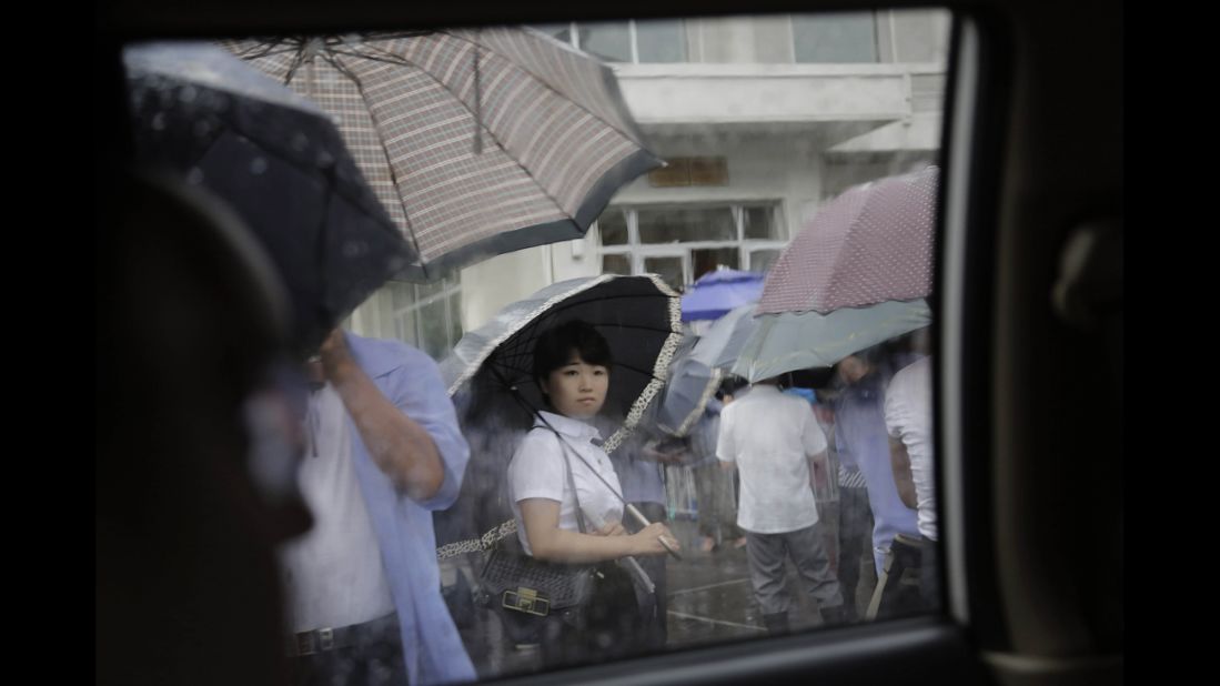 A woman waits outside a restaurant in the rain.
