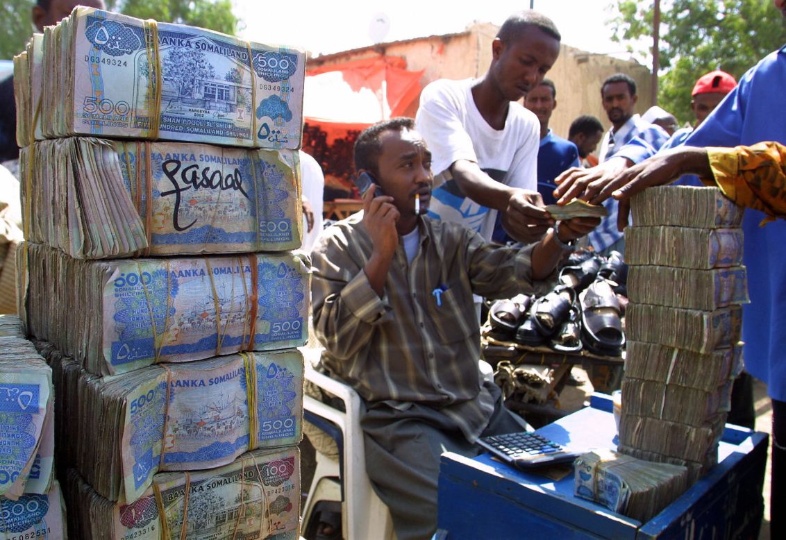 Somali money changer next to piles of banknotes on a busy street in Hargeisa.