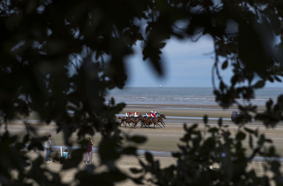A view of the action as riders and jockeys come into view through a gap in trees above the beach.