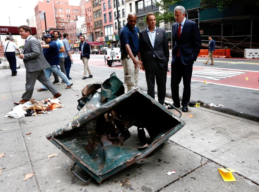 New York Mayor Bill de Blasio, right, and New York Gov. Andrew Cuomo, second right, look over the mangled remains of a dumpster Sunday, September 18, in New York's Chelsea neighborhood. An explosion injured 29 people there the night before.
