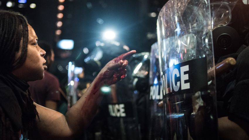 With blood covering her hand and arm, a woman points at a police officer on September 21 in Charlotte, North Carolina. The North Carolina governor has declared a state of emergency in the city of Charlotte after clashes during protests in the city in response to the fatal shooting by police officers of 43-year-old Keith Lamont Scott at an apartment complex near UNC Charlotte.