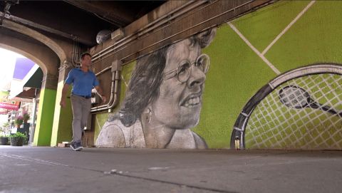 The competition was founded by Billie Jean King. Here Open Court host Pat Cash walks past a mural of the US tennis legend during CNN's visit to Forest Hills.