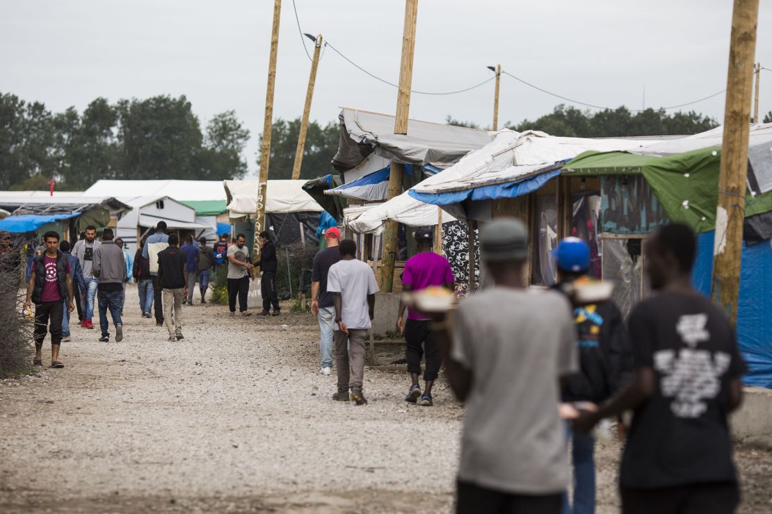 Migrants walk past make-shift shops and shelters by the Jungle Books Cafe at the Jungle migrant camp in Calais, France.