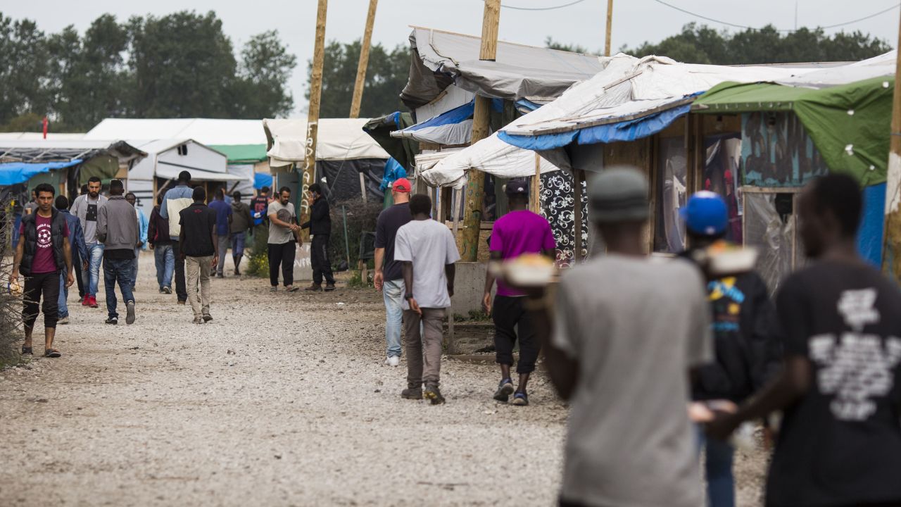 Migrants walk past make-shift shops and shelters by the Jungle Books Cafe at the Jungle migrant camp in Calais, France.