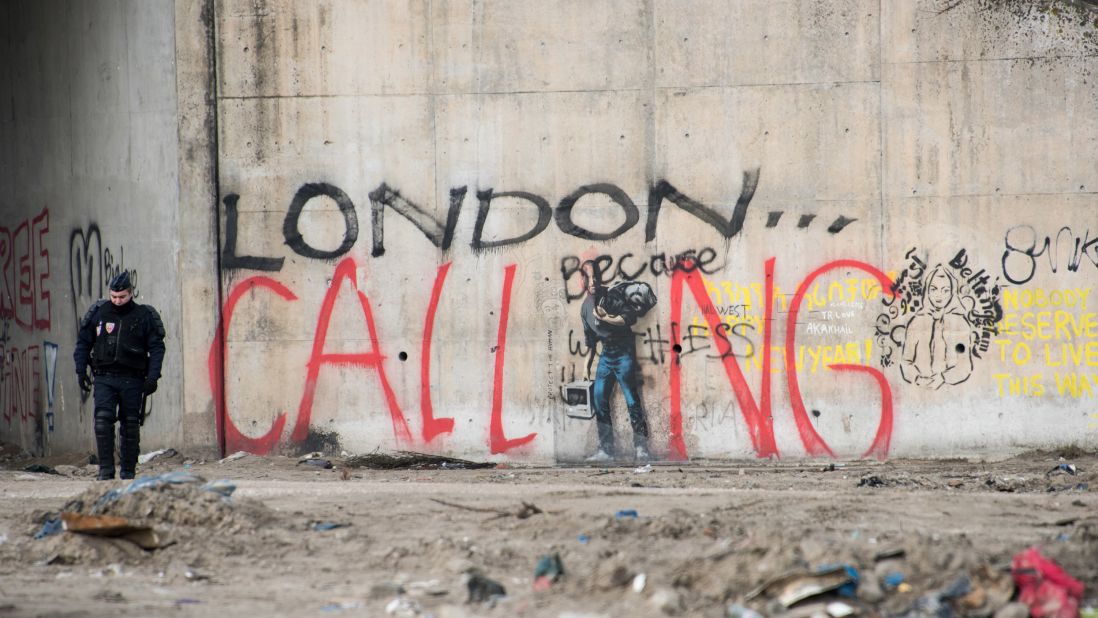 A French riot policeman stands near graffiti during the dismantling of the southern part of "The Jungle" migrant camp on Thursday, March 10. The graffiti reads "London calling," a reference to how the camp has become notorious for migrants and refugees trying to enter the UK illegally.