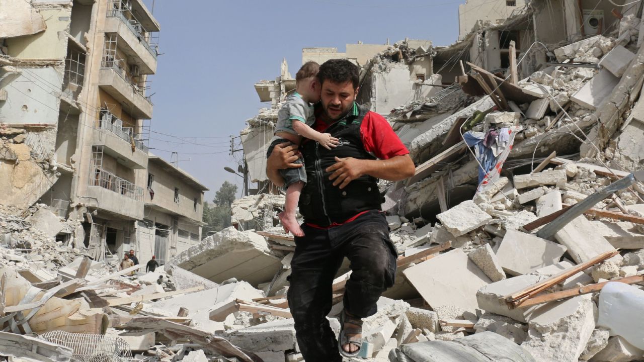 A Syrian man carries a baby after removing him from the rubble of a destroyed building.