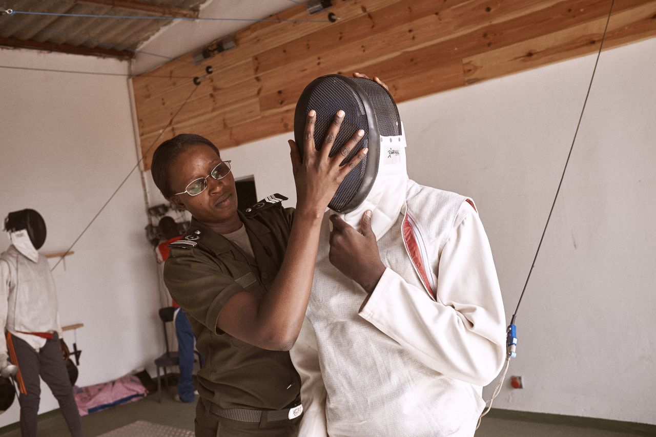 Prison guard Fatoumata Sy assists a boy with his mask."Fencing "is a discipline," says Sy. "We try to transmit these rules to show that in a group, in society there is a discipline, there are laws that you have to respect."<br />