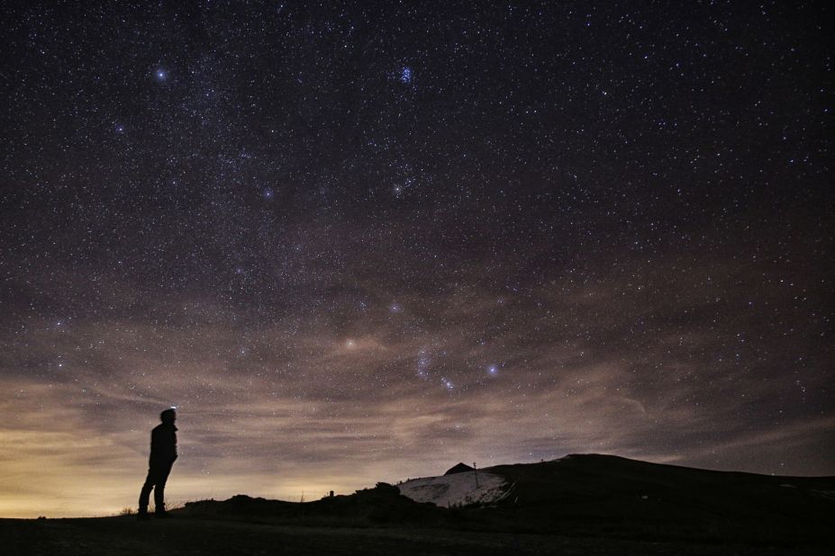 A photographer looks at the sky at night in northern Italy during the 2015 Geminid meteor shower.