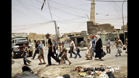 Moslawis walk past trash strewn about a busy market area in Mosul in 2009. 