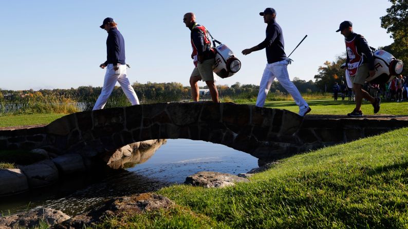 Brandt Snedeker and Brooks Koepka of the United States walk across the bridge on the seventh hole with their caddies.