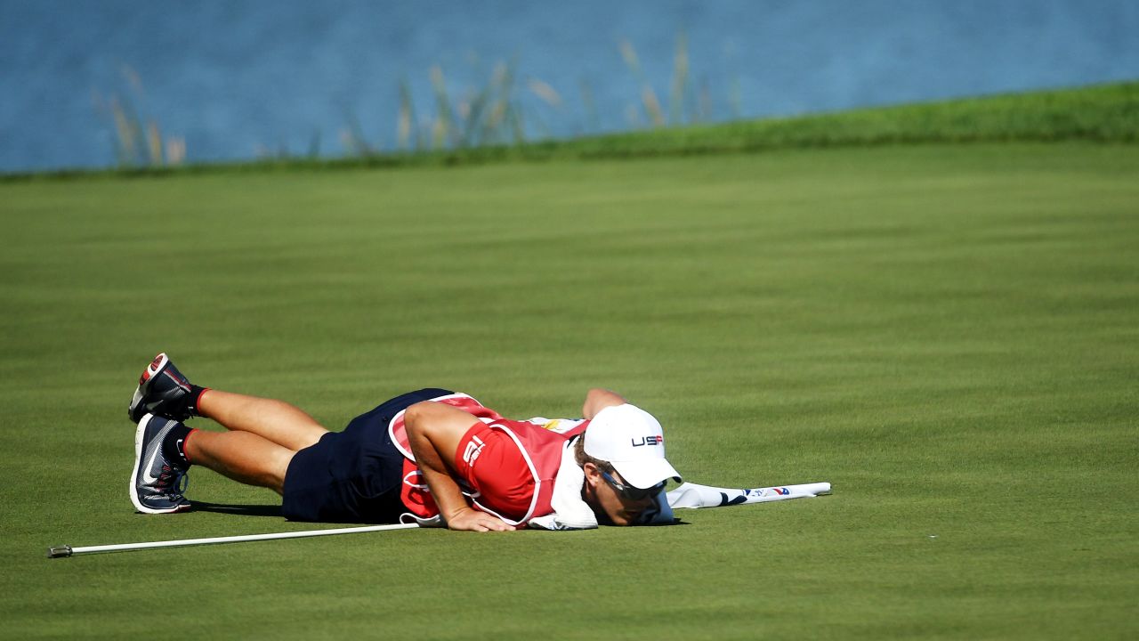 The caddie for Patrick Reed of USA, Kessler Karain, checks the line for a putt on the seventh green.