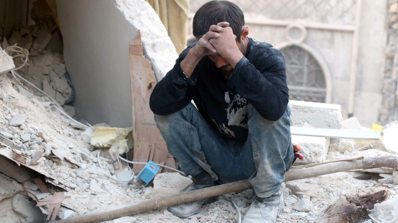 A Syrian man reacts as he sits on the rubble of destroyed buildings in Aleppo.