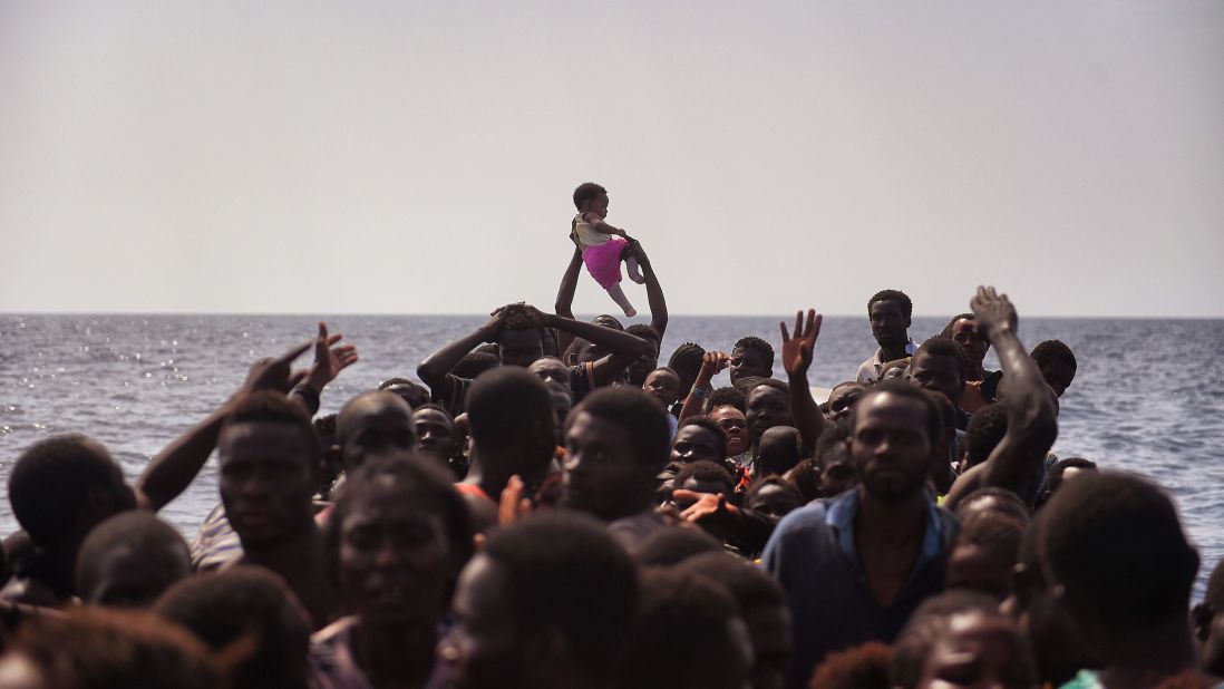 A child is lifted above the crowded boat as migrants wait to be rescued.