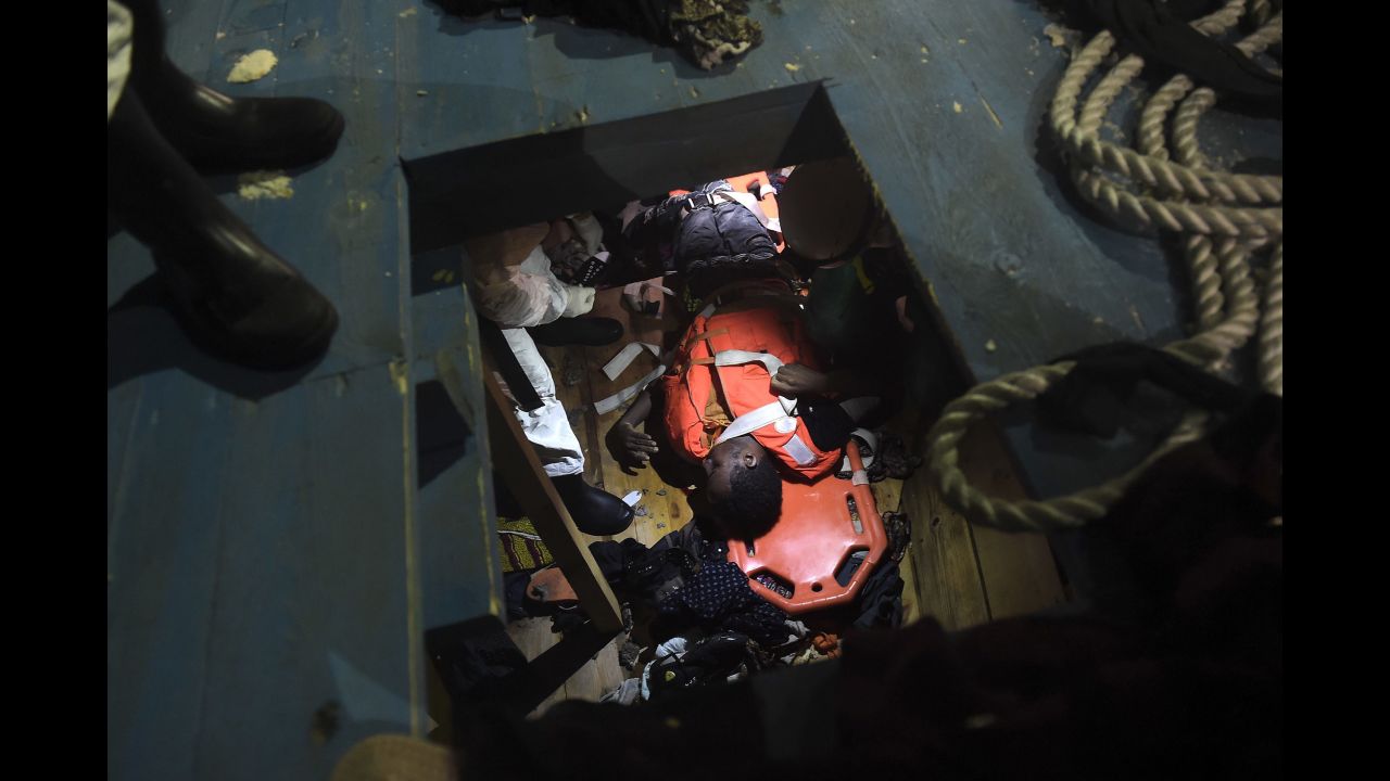 Members of Proactiva Open Arms NGO prepare to evacuate a body on a stretcher from the third level of a wooden vessel.