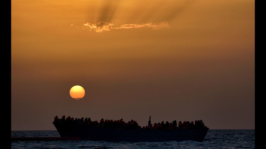 Migrants wait to be rescued as they drift at sunset in the Mediterranean Sea.