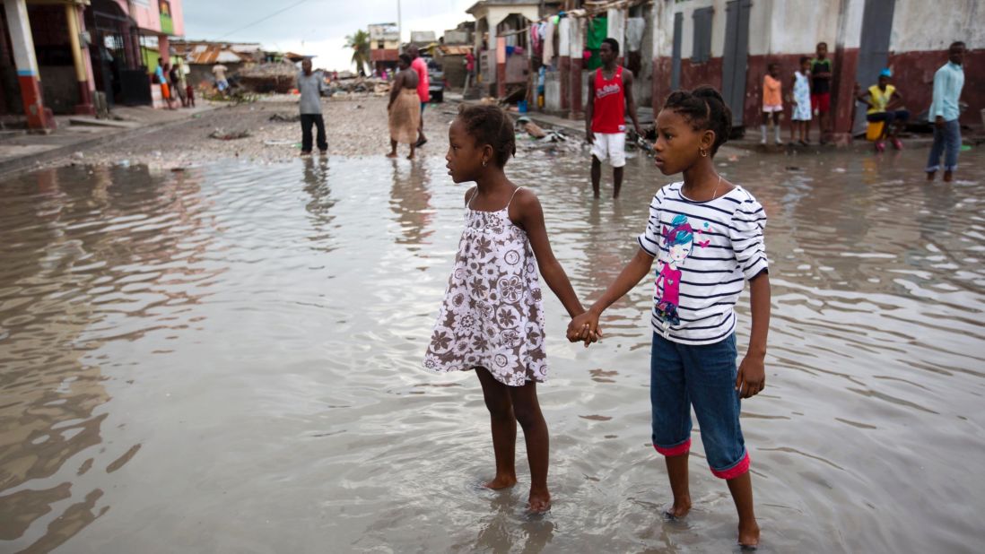 Girls hold hands as they help each other wade through a flooded street in Les Cayes on October 6.