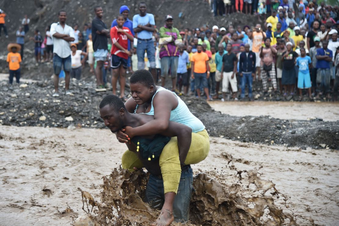 A man carries a woman across a  river where a bridge collapsed near Port-au-Prince. Hurricane Matthew has killed at least 108 people in Haiti. 