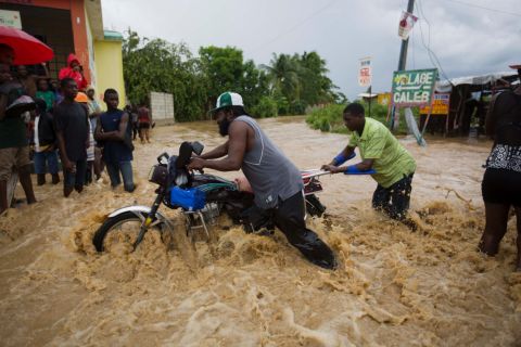 Men push a motorbike through a flooded street in Leogane on October 5. More than 300,000 people are in shelters across the country, the United Nations said.<br />
