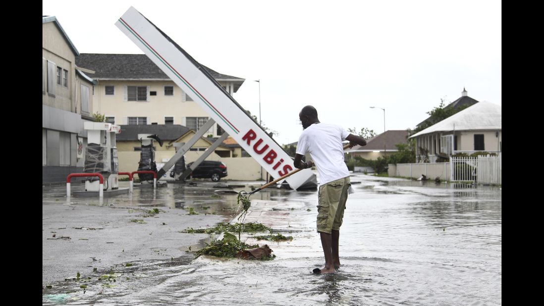 A man rakes up debris from a storm drain as he begins cleanup near a damaged gas station in Nassau on October 6.