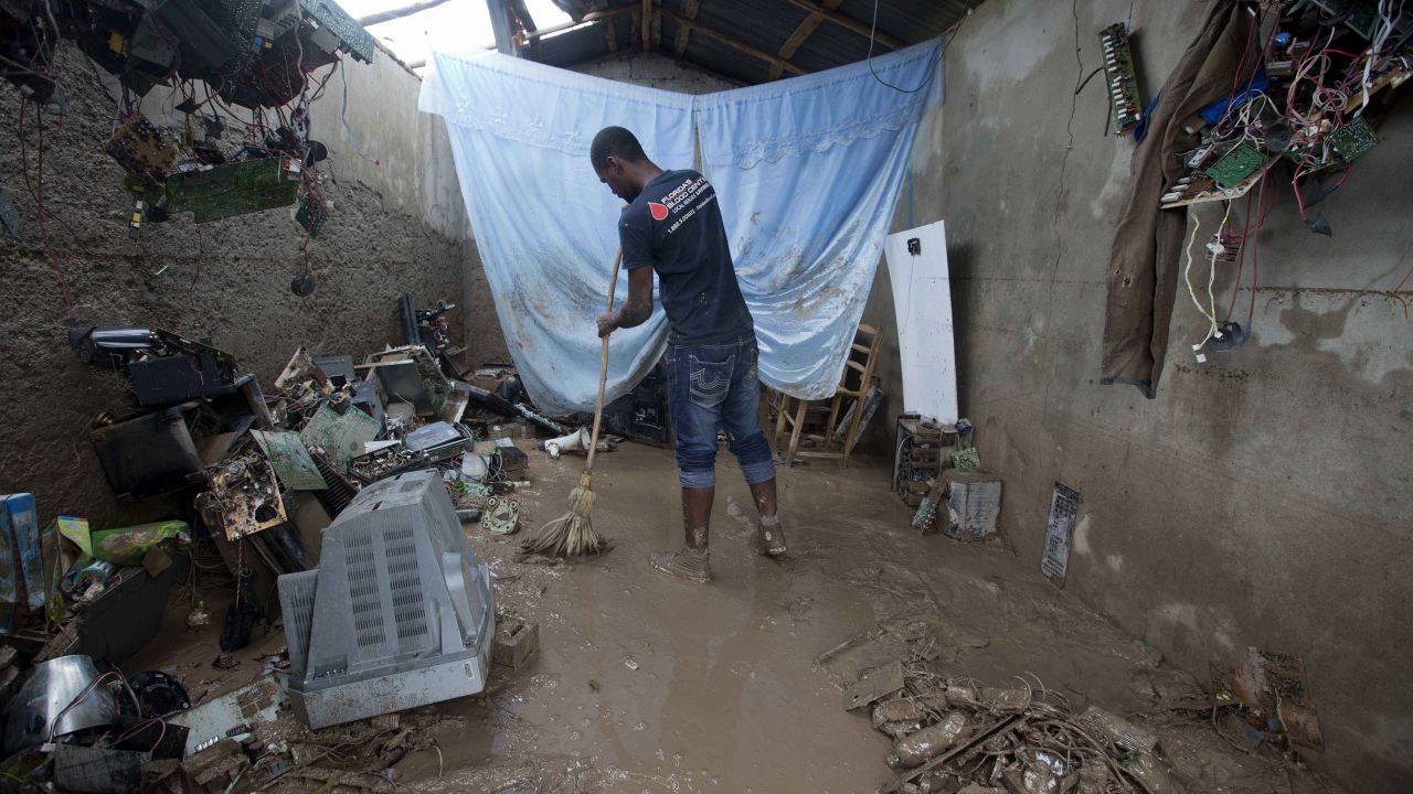 A man cleans his destroyed office, which is filled with thick mud.