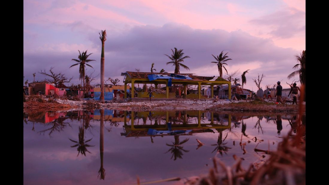 People pass damaged buildings in a seaside fishing neighborhood of Port Salut on Sunday, October 9.