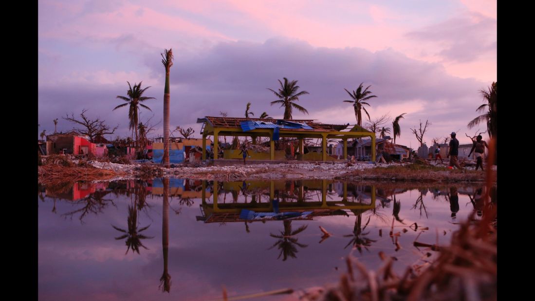 People pass damaged buildings in a seaside fishing neighborhood of Port Salut on Sunday, October 9. 