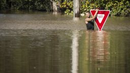 A man holds onto a yield sign after trying to swim out to help a stranded truck driver at NC 301 Highway and Tom Starling Road in Hope Mills, North Carolina on October 9. Both people were rescued.