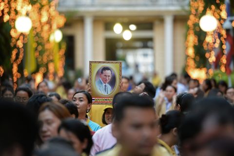 A portrait of the King is held on the eve of his 88th birthday as people gather outside the Siriraj hospital in 2015. The King of Thailand is regarded as a demi-god by many Thais, and his popularity has been viewed as a unifying force during times of political unrest.