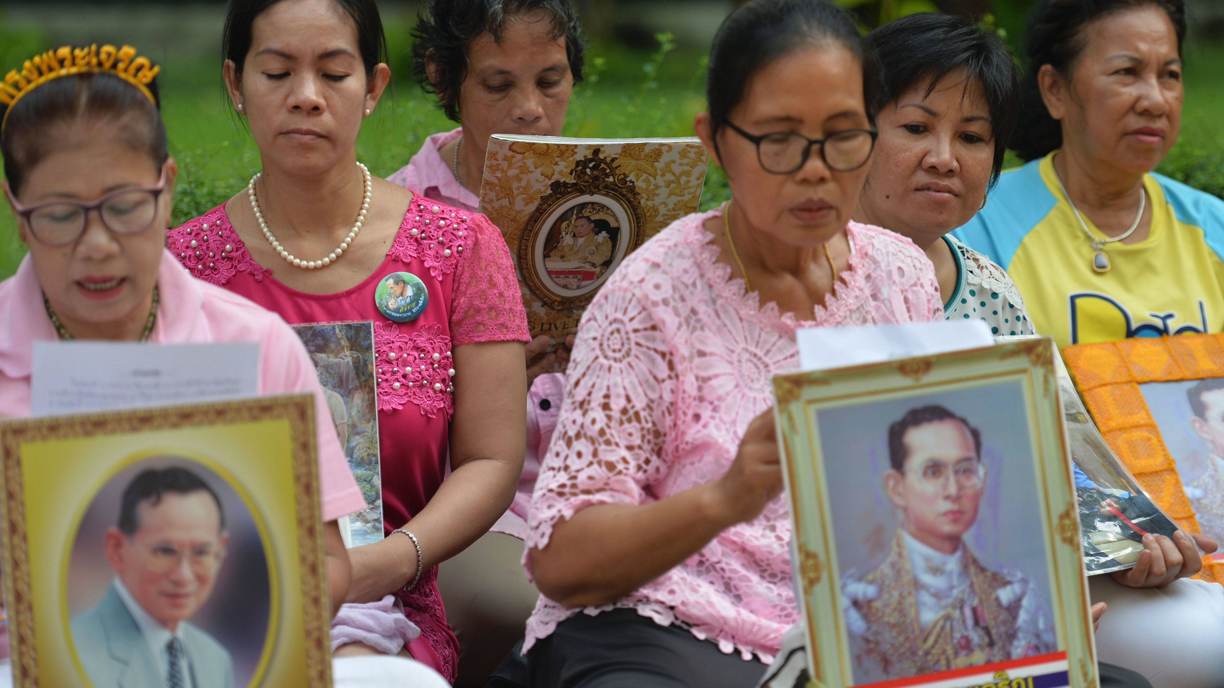 Women hold portraits of Thai King Bhumibol Adulyadej as they pray for his health at Siriraj Hospital in Bangkok on October 12, 2016.