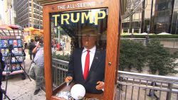 Meet Trump the Fortune Teller. Jeanne Moos reports animatronic Trump is attracting crowds.    Fortune Teller Trump   The Donald now has a crystal ball and is telling fortunes. The All Seeing Trump is popping up in front of places like Trump Tower and Fox News. And on Wednesday we got a chance to fool around with him as he attracted a crowd of laughing spectators outside the Trump International Hotel. He's an animatronic likeness of the Donald inside a booth. He makes funny predictions about the future (the predictions mock the Donald's positions) and hands out written "misfortunes." He's modeled after "Zoltar", the fortune teller in the Tom Hanks' movie "Big." The All Seeing Trump was the brain child of anonymous Brooklyn artists and is voiced by a comedian impersonating Trump.  Cost to build it...$9000. When they set it up outside Trump Tower, there's video of clueless security looking at it in bewilderment. Finally the police turned off the sound to shut it up. Click link below to hear it.