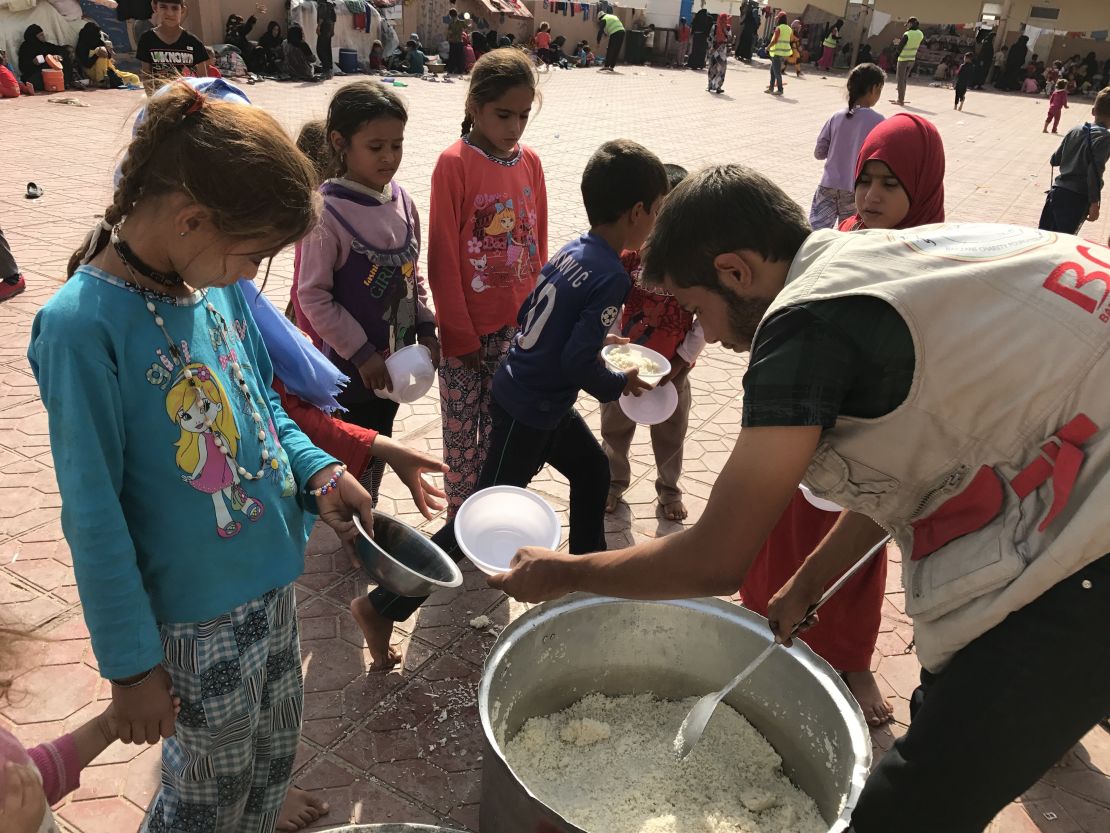 An aid worker hands out dishes of food to displaced Iraqi children at Debaka Camp.