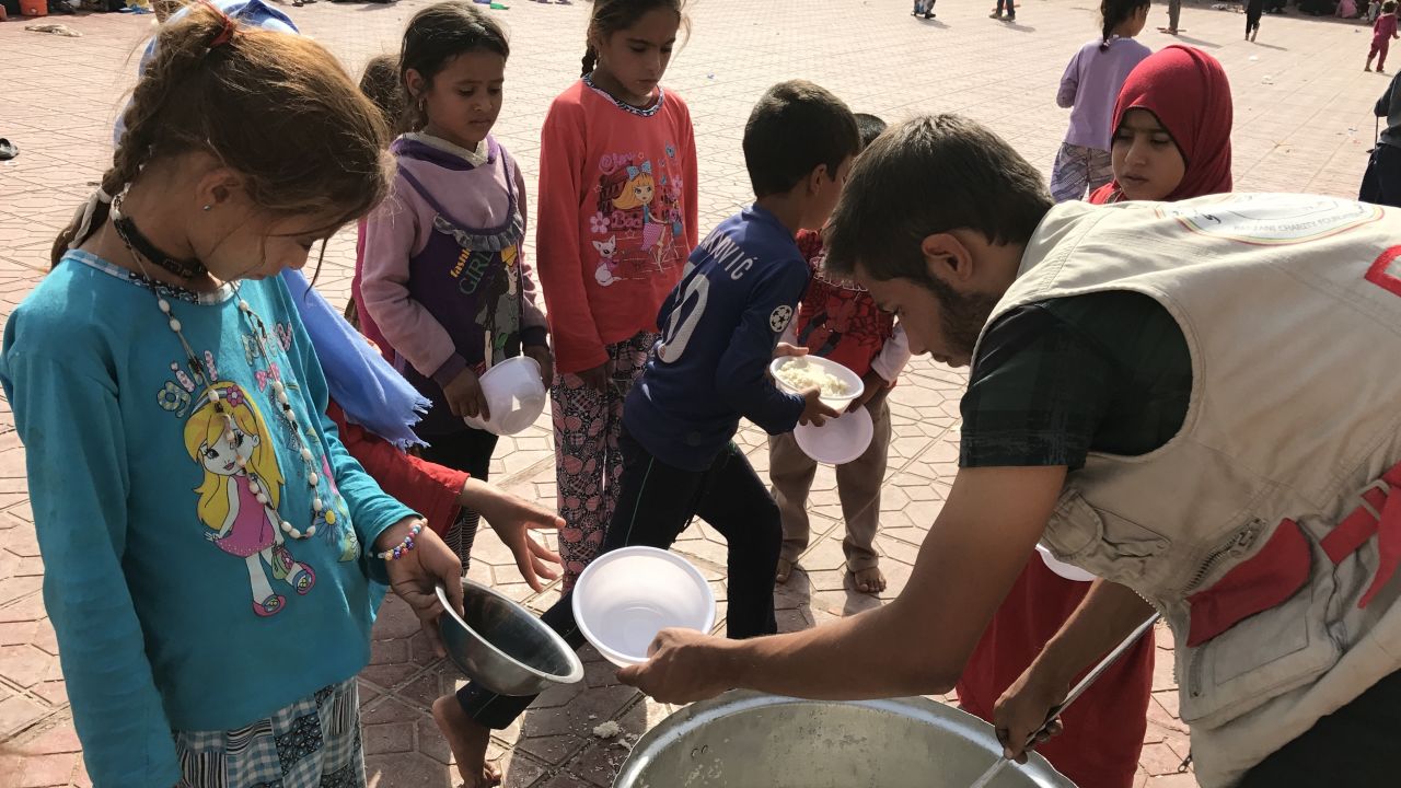 An aid worker hands out dishes of food to displaced Iraqi children at Debaka Camp.