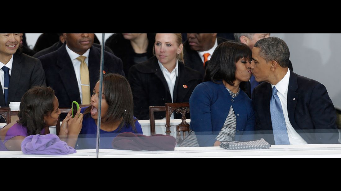 Obama kisses his wife during the inaugural parade in Washington. Sasha, left, takes a photo of her sister, Malia.