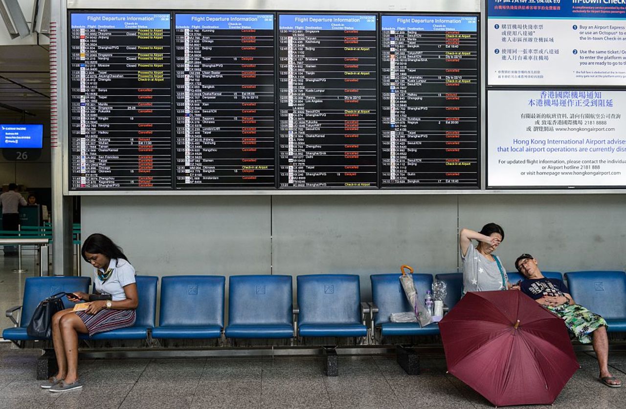 People wait under displays showing lists of canceled and delayed flights at the Airport Express station as Typhoon Haima approaches Hong Kong.