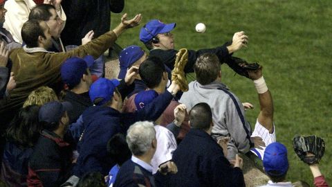 On October 14, 2003, Cubs left fielder Moises Alou's arm reaches into the stands unsuccessfully for a foul ball tipped by fan Steve Bartman, wearing headphones and glasses.