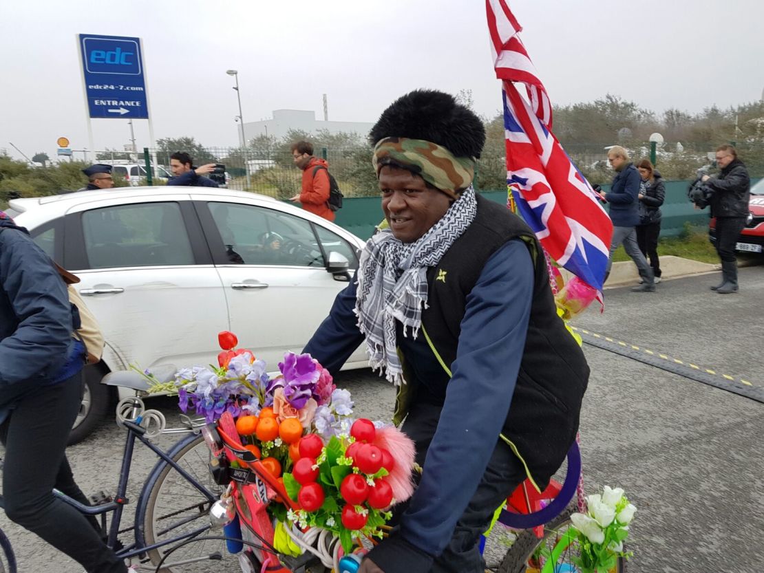 An Eritrean migrant rides by a processing center in Calais as authorities prepare to raze the infamous "Jungle" refugee camp.