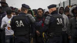 CALAIS, FRANCE - OCTOBER 24: Migrants queue behind a line of police at a reception point outside the Jungle migrant camp before boarding buses to refugee centres around France on October 24, 2016 in Calais, France. French authorities have begun to clear the estimated 7000 people from the Jungle migrant and refugee camp ahead of its demolition. (Photo by Jack Taylor/Getty Images)