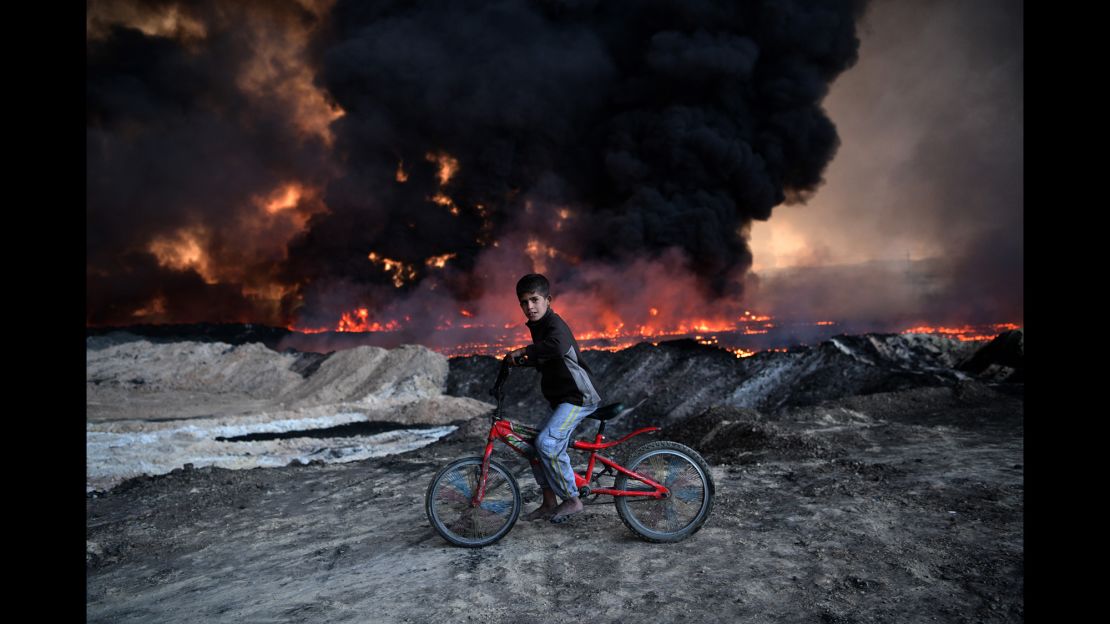 A boy pauses on his bike as he passes an oil field that was set on fire by retreating ISIS fighters ahead of the Mosul offensive, on October 21 in Qayyara.