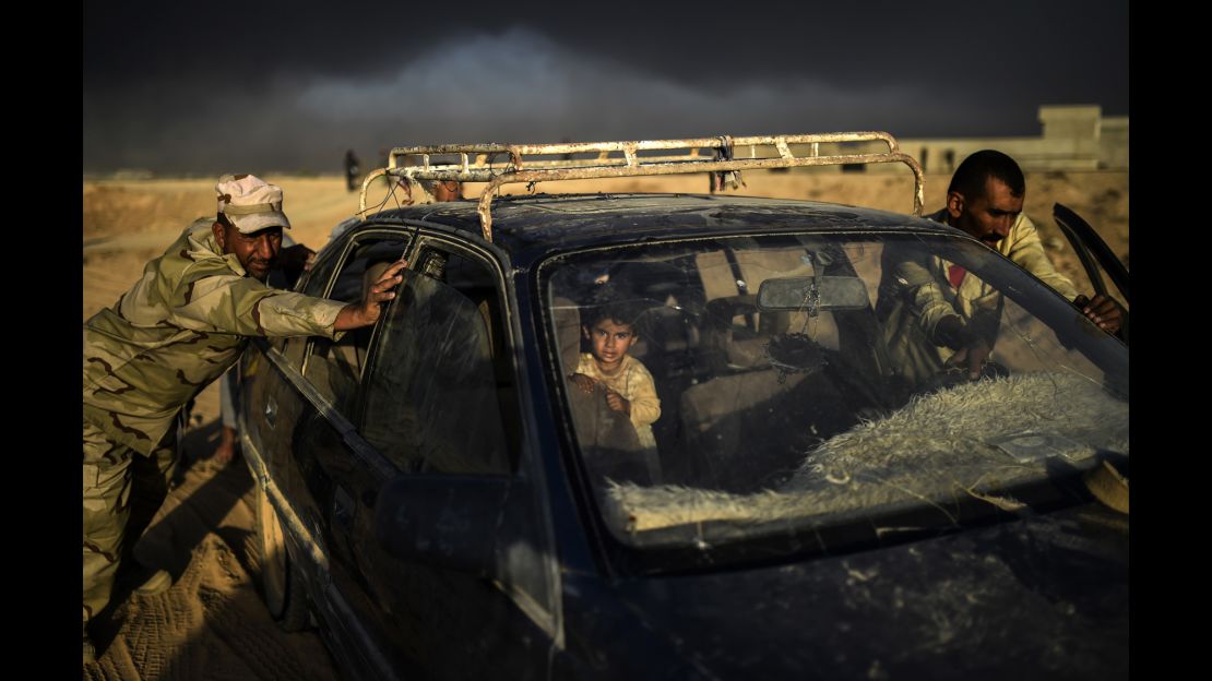 An Iraqi forces member helps a man push a car as they arrive at a refugee camp on October 22, in the town of Qayyara.