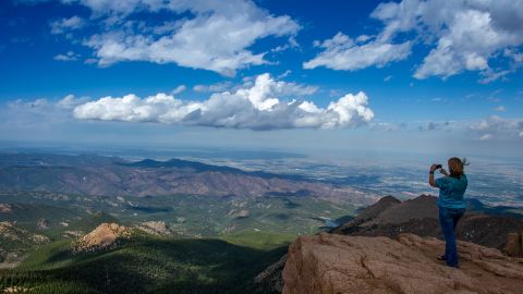 A woman takes a picture at the top of Pikes Peak mountain in the Rocky Mountains.