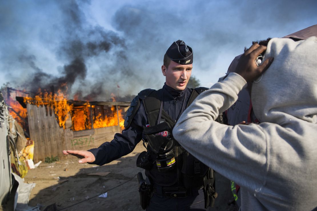 A police officer stands guard after migrants burn down a shelter as authorities move in to clear the camp on Tuesday.