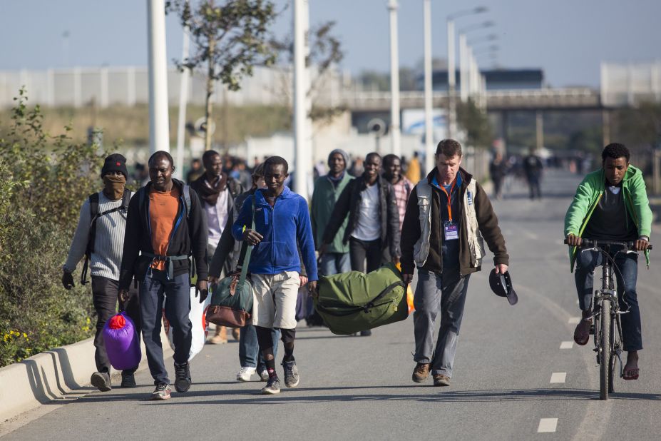 A volunteer helps a man carry his luggage away from the camp on October 25.