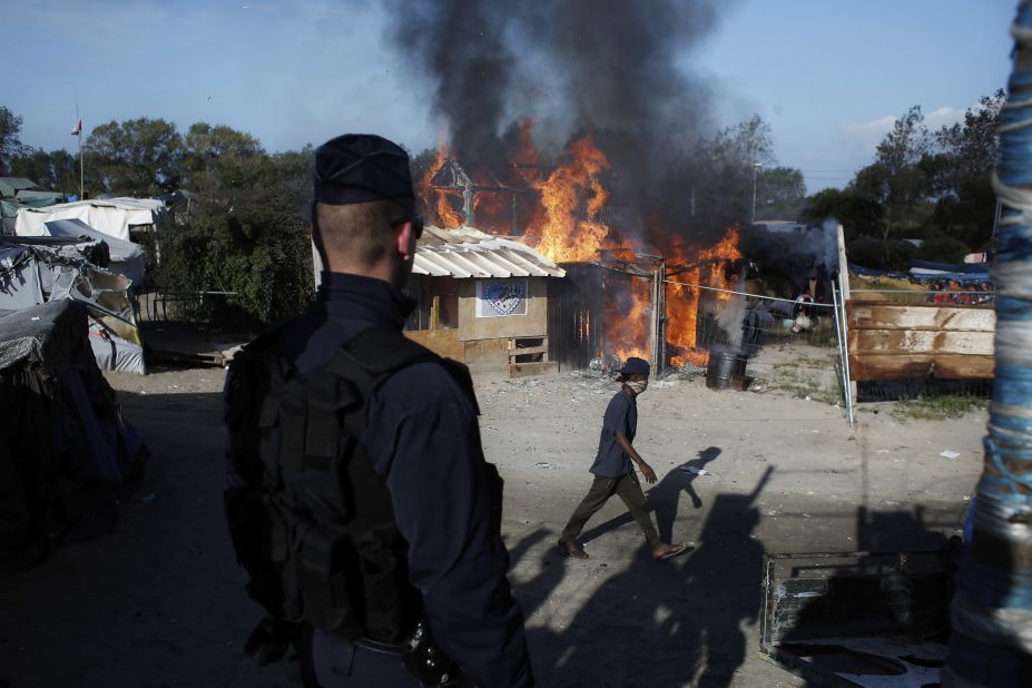 A man passes a camp structure on fire on October 25.