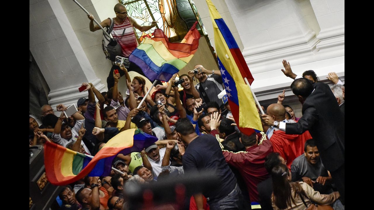 Supporters of President Nicolas Maduro wave flags and shout as they force their way into the National Assembly floor during a meeting of the opposition-led congress in Caracas on Sunday, Oct. 23, 2016. The four-hour extraordinary session was interrupted for about 30 minutes after government supporters breached security and threatened lawmakers on the National Assembly floor.