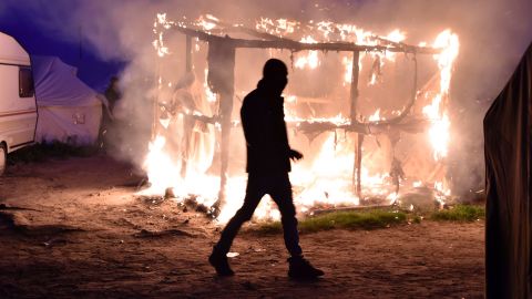 A migrant walks past a shack set ablaze on Tuesday night.