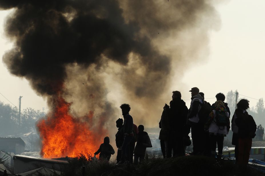 Remaining migrants watch fires burn across the Jungle on October 26. Migrants set fire to structures along the camp's main street.