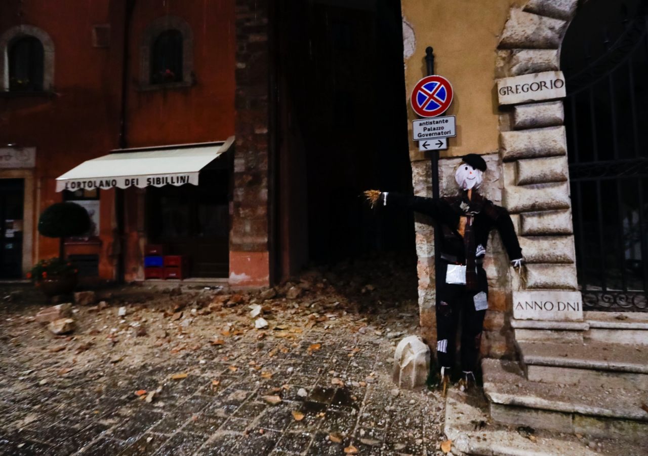 A Halloween dummy rests on a wall in front of earthquake damage in Visso.