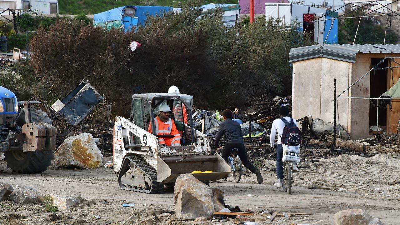 Two people cycle past a man driving a bulldozer in The Jungle camp in Calais, on October 27, 2016.