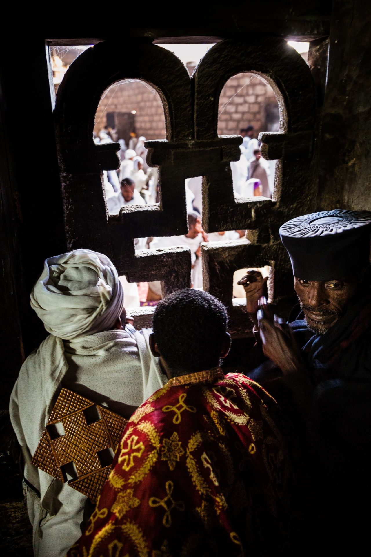 Here the priests of Lalibela look out of an intricately carved window of their church to the crowds below. Every church in Lalibela has a resident priest who wears ornate brocade robes and carries a large processional cross.