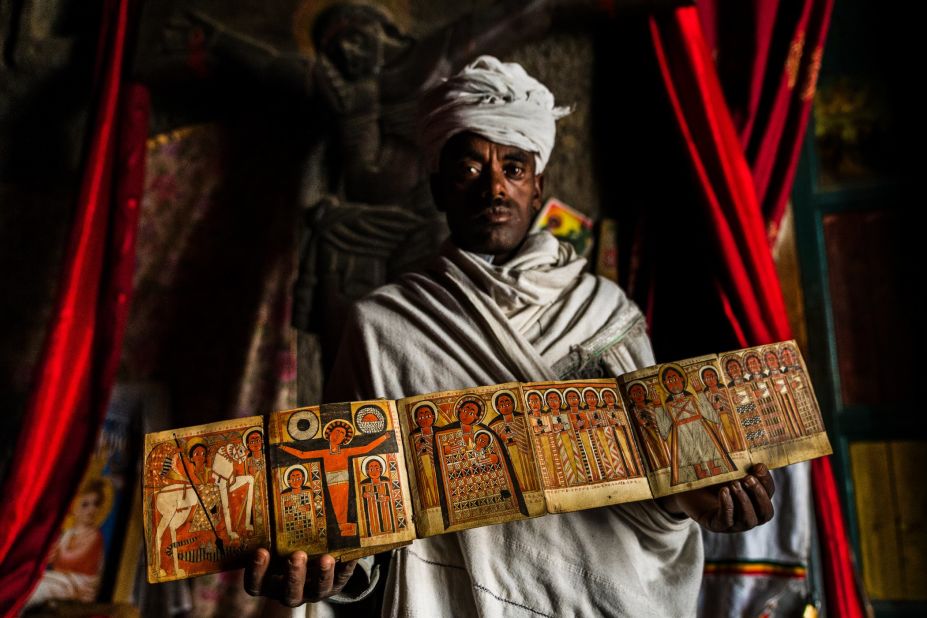 A priest from a church in Lalibela shows off an illuminated manuscript depicting Jesus, St George and other religious figures. Behind him is an intricate crucifix carved out of stone. The 13 churches of Lalibela are home to some of Ethiopia's most sacred artifacts.